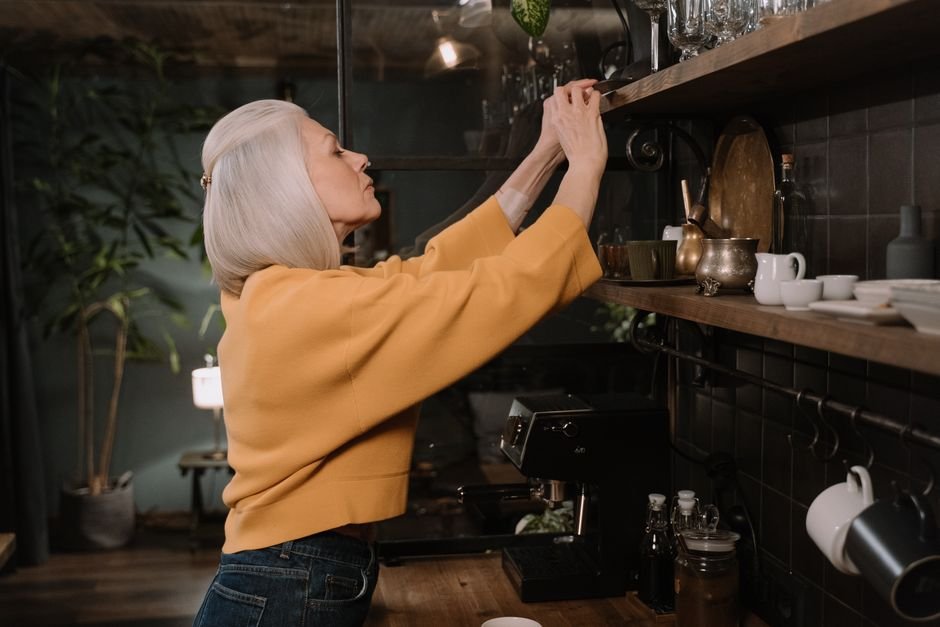 Elderly woman reaching for an item on a kitchen shelf
